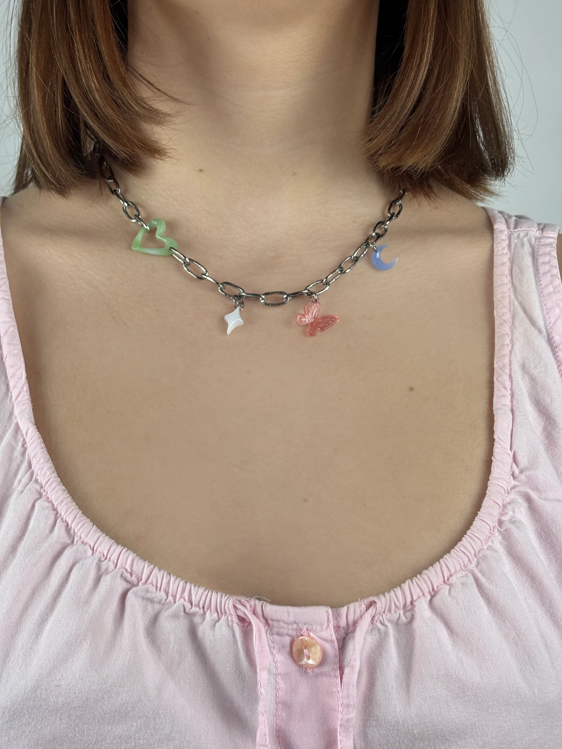 Collier gros maillon argenté avec quatre charms. Une coeur vert ajouré, une étoile blanche, un papillon rose et une lune bleue claire.