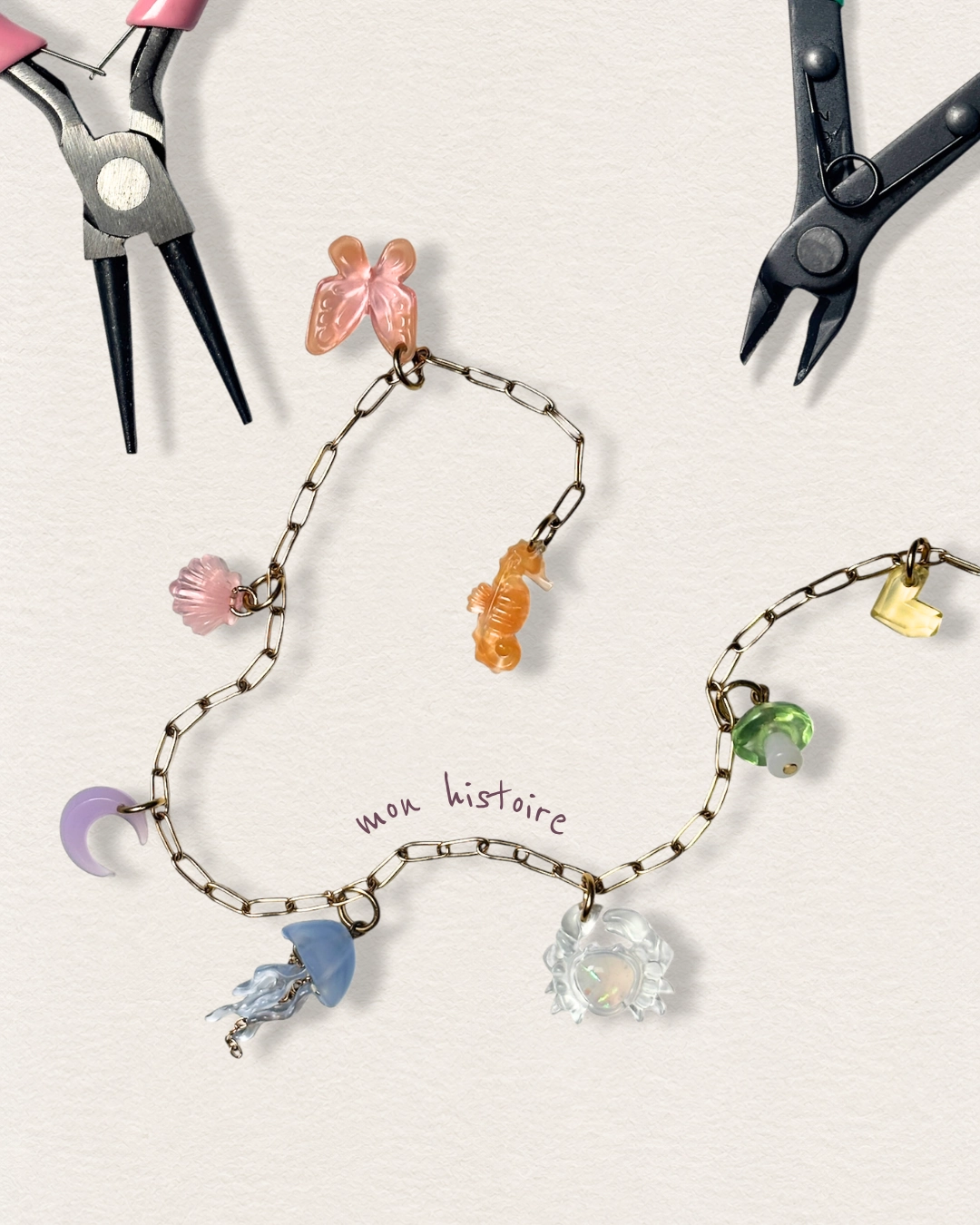 Création artisanale d’un bijou à charms personnalisable Odyssée Bijoux : charms marins hippocampe, méduse, crabe et coquillage sur chaîne dorée avec pinces de bijoutier
