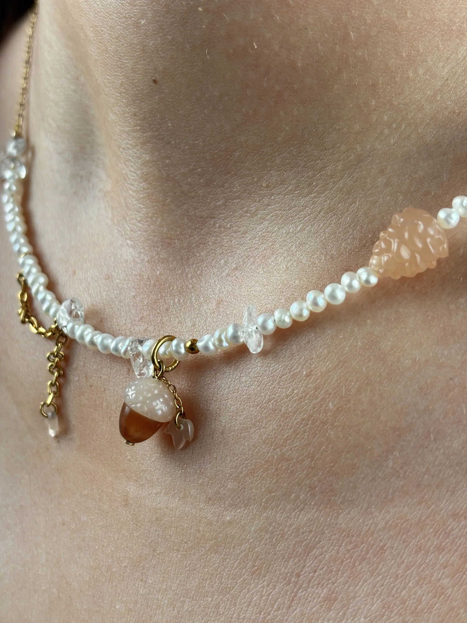 Gros plan du collier Forêt porté : charm gland, charm pomme de pin et perles d'eau douce
