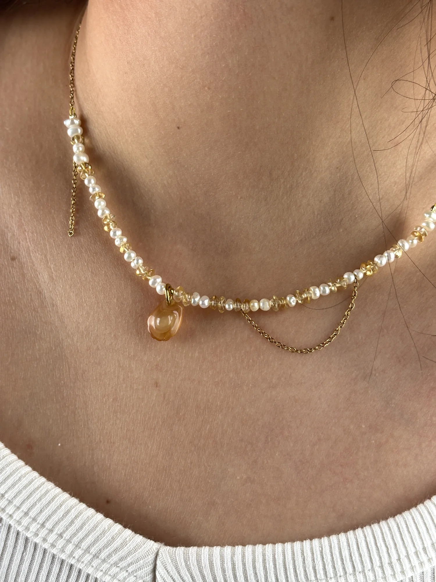 Gros plan du collier Madeleine doré porté : charm madeleine couleur miel, perles d'eau douce, citrine et chaîne en drapé