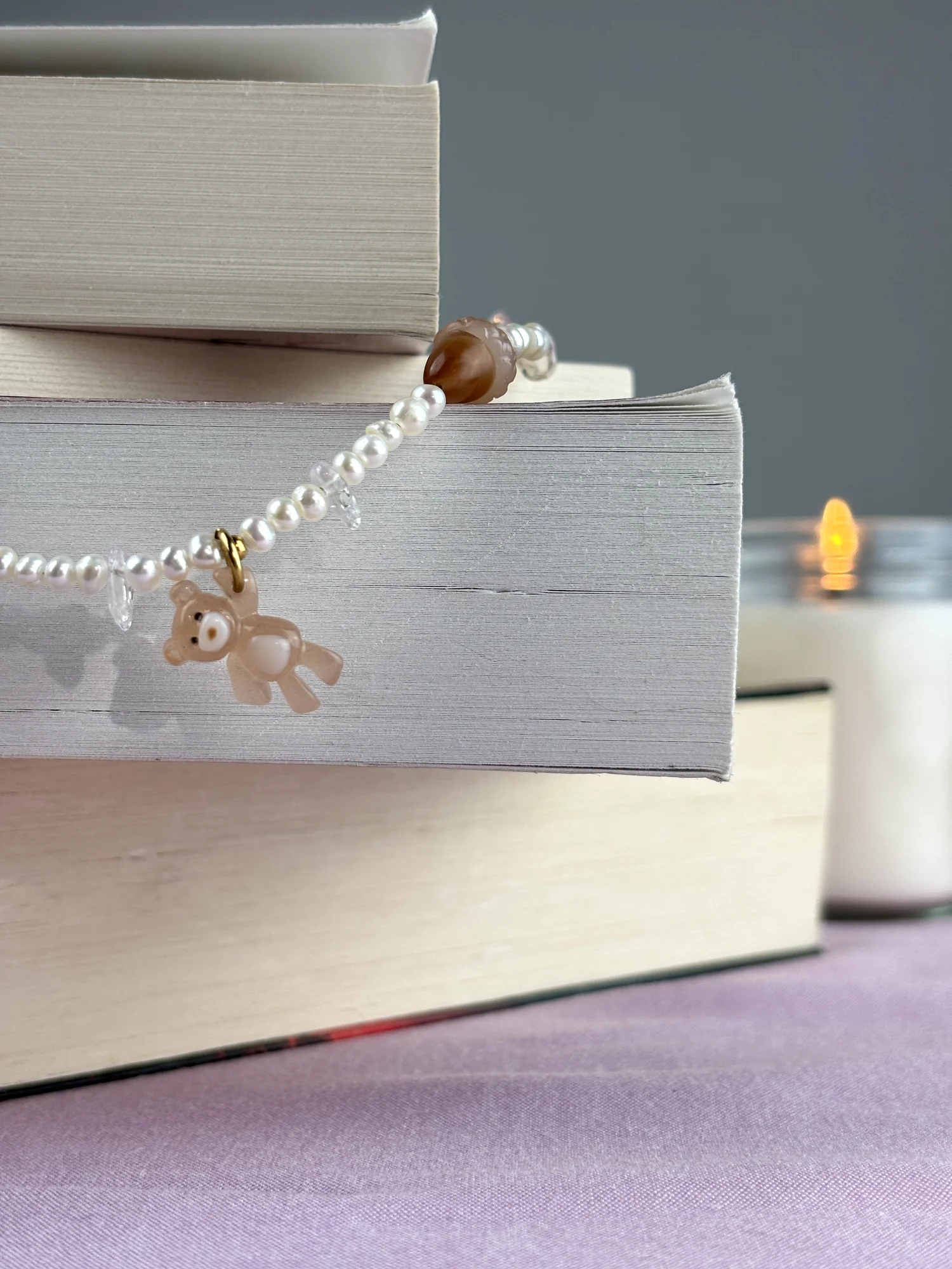 Charm ourson brun du collier Ourson Brun posé sur une pile de livres, bougie allumée en arrière-plan